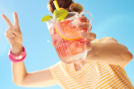 Closeup on refreshing cocktail in the hands of young woman showing victory against blue skyの写真素材
