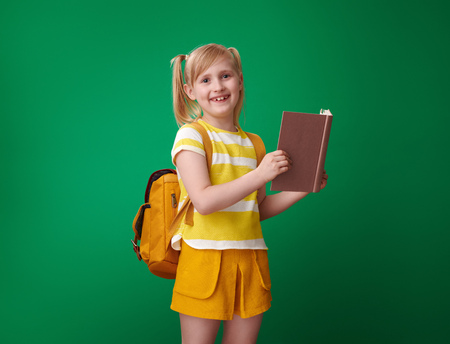 smiling school girl with backpack reading a book isolated on green backgroundの写真素材