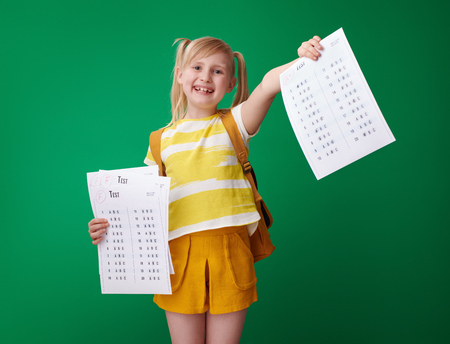 smiling school girl with backpack showing an excellent grade test after several failures on green backgroundの写真素材