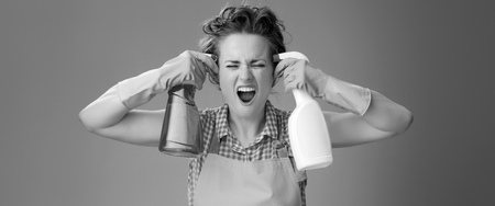 Big cleaning time. stressed modern housewife with rubber gloves wanting to shoot herself from a bottles of detergent isolated on backgroundの写真素材