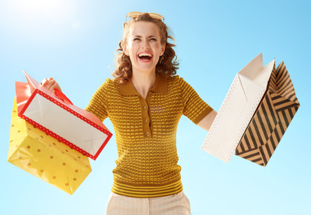 Cheerful stylish woman with shopping bags against blue sky