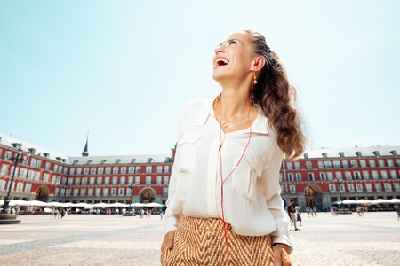 smiling young woman at Plaza Mayor looking into the distance and listening to an audio guideのeditorial素材