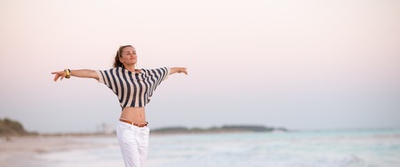 trendy woman in white pants and striped shirt on the seacoast in the evening rejoicingの写真素材