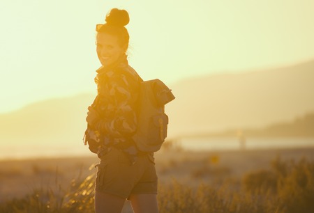 happy active tourist woman in hiking gear against mountain and sea landscape at sunsetの写真素材