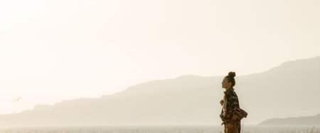 fit tourist woman in hiking clothes against mountain and ocean landscape at sunset