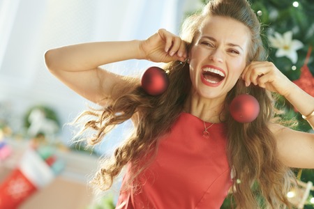 happy young woman in red dress near Christmas tree having fun timeの写真素材