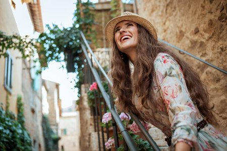 happy modern traveller woman in long dress and straw hat in Pienza, Italy having fun time