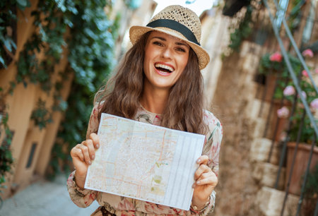 smiling stylish traveller woman in long dress and straw hat with map in old Italian town