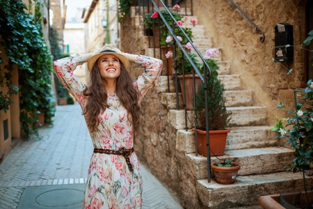smiling trendy traveller woman in long dress and straw hat in old Italian town having excursionの写真素材