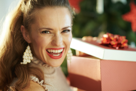 Portrait of happy modern housewife near Christmas tree opening Christmas present boxの写真素材
