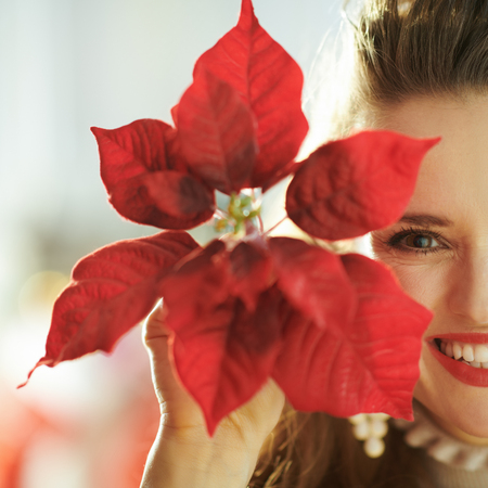 smiling modern woman near Christmas tree showing red poinsettiaの写真素材