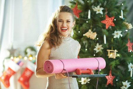 smiling trendy housewife with fitness gear near Christmas treeの写真素材