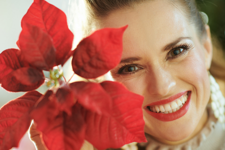 smiling modern woman near Christmas tree showing red poinsettiaの写真素材