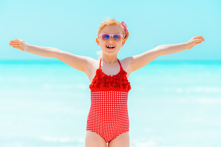 happy modern child in red swimsuit on the seashore rejoicingの写真素材