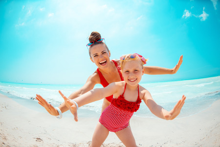 happy young mother and daughter in red swimsuit on the seacoast having fun timeの写真素材