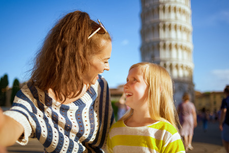 smiling modern mother and daughter taking selfie against leaning tower in Pisa, Italy. classic place to take photos for social media platform. daughter with blond hair . well know touristed path.の写真素材