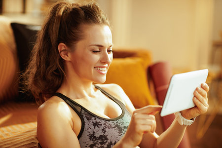 smiling active woman in sport clothes in the modern house watching fitness tutorial on internet via...