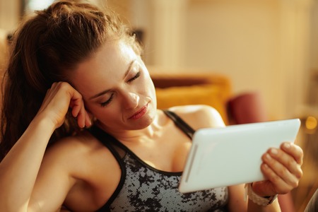 tired fit sports woman in fitness clothes at modern home fall asleep while watching fitness tutorials on internet via tablet PC.の写真素材