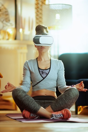 relaxed active woman in sport clothes at modern home doing yoga in VR gear.の写真素材