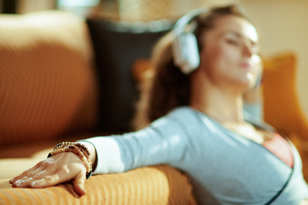 Closeup on relaxed active woman in fitness clothes listening to the music with headphones at modern home.の写真素材