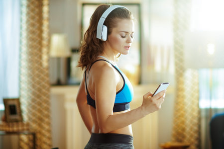 fit sports woman in headphones in sport clothes at modern home using online fitness training program...