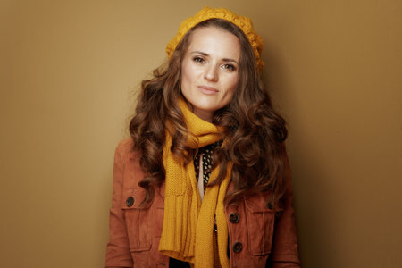 Hello autumn. Portrait of middle age woman in yellow beret and scarf against brown background.