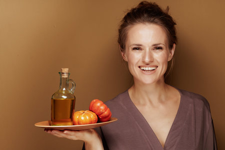 Hello autumn. Portrait of happy elegant 40 year old woman in a bathrobe showing pumpkin oil against...