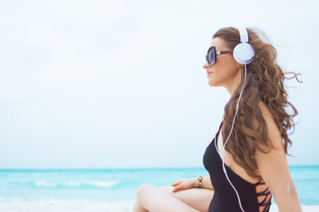 stylish 40 year old woman with long curly hair in elegant black bathing suit looking into the...