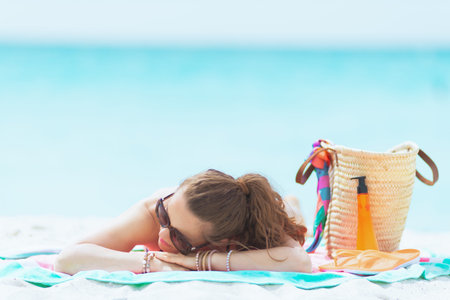 relaxed stylish 40 year old woman with long curly hair in elegant black swimsuit on a white beach...