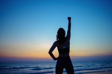 Seen from behind healthy woman in fitness clothes on the seacoast in the evening rejoicing.の写真素材