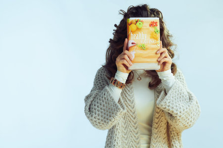 young woman with long wavy hair in neck sweater and cardigan holding healthy eating book in the...