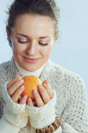 happy stylish woman in roll neck sweater and cardigan holding orange against winter light blue background.の写真素材