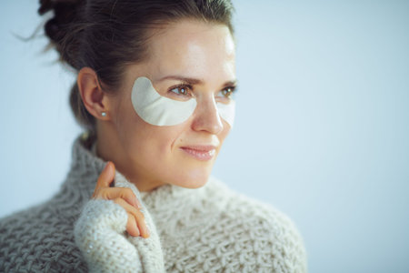 relaxed modern middle age woman in roll neck sweater and cardigan with cosmetic eye patches as part...