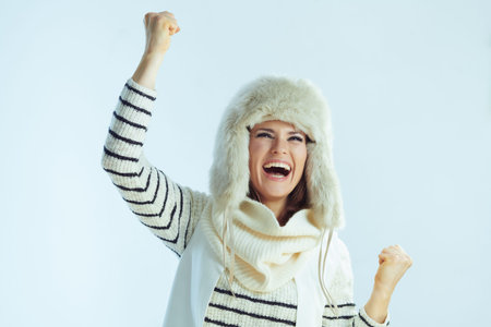 smiling stylish 40 years old woman in white striped sweater, scarf and ear flaps hat rejoicing on...