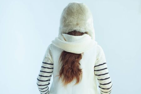 Seen from behind modern 40 years old woman in white striped sweater, scarf and ear flaps hat on winter light blue background.の写真素材