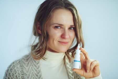 Portrait of sick modern housewife in roll neck sweater and cardigan showing nasal spray isolated on winter light blue background.の写真素材