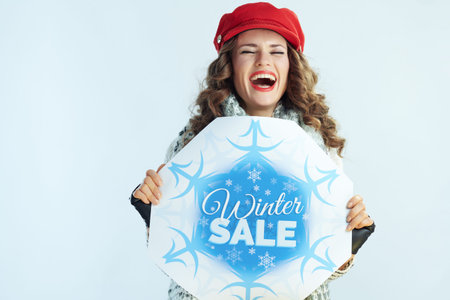 cheerful stylish middle age woman with long brunette hair in sweater, scarf and red hat holding...