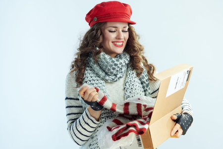 happy young woman with long brunette hair in sweater, scarf and red hat holding opened parcel and...