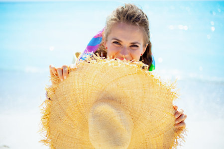 happy modern woman in white t-shirt hiding behind with big straw hat on the seacoast.