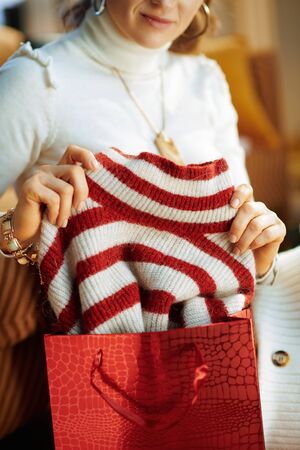 Closeup on young female in white sweater and skirt with shopping bags checking bought sweater in the modern house in sunny winter day.の写真素材
