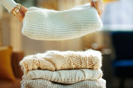 Closeup on modern female in white sweater and skirt at modern home in sunny winter day prepare sweaters pile for storage.の写真素材
