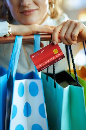 Closeup on young woman in white sweater and skirt with credit card near colorful shopping bags hanging on copper clothes rail.の写真素材