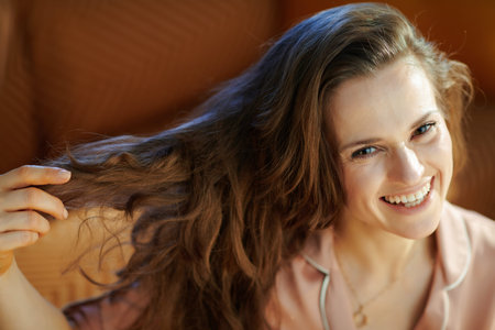 happy young housewife in pajamas with long brunette wavy hair in the modern living room in sunny...