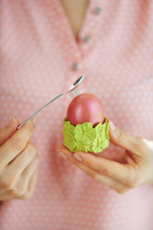 Closeup on housewife beat red easter egg in green egg cup with spoon in the living room in sunny spring day.の写真素材