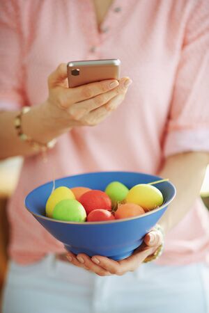 Closeup on woman taking photo with smartphone of with a blue plate with colorful easter eggs in the living room in sunny spring day.の素材 [FY310142332372]