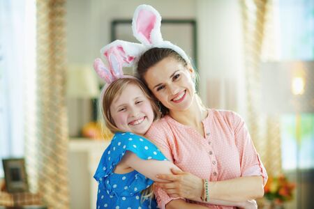 Portrait of happy modern mother and child in easter bunny ears in the modern living room in sunny spring day embracing.の写真素材