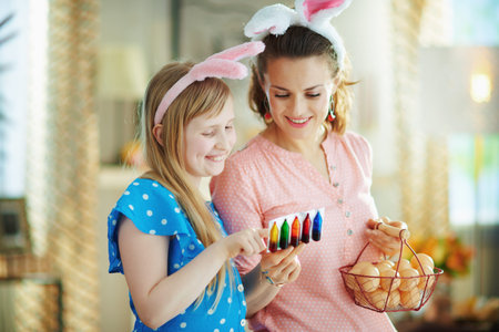 happy young mother and child in easter bunny ears with basket with farm eggs and food coloring...