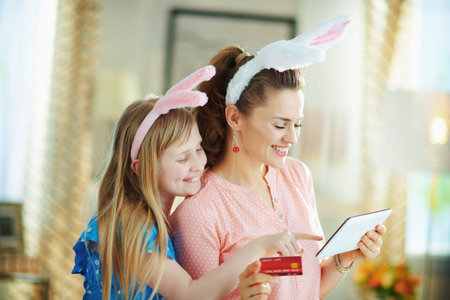 happy elegant mother and daughter in easter bunny ears with credit card buying online on a tablet PC...