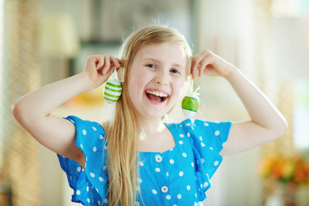 happy modern child in a polka dot blue overall and easter bunny ears making earrings with green...
