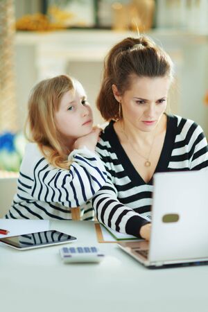 bored child craving attention while mother busy working in home office in the modern house in sunny day.の写真素材